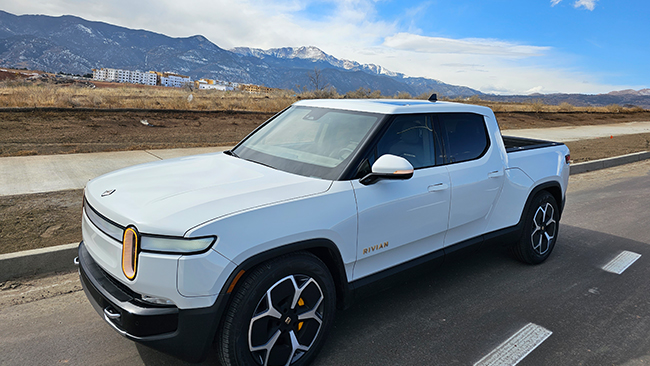 A picture of Jeff's white Rivian R1T pickup truck parked along the road, with a mountain and small town in the backdrop.