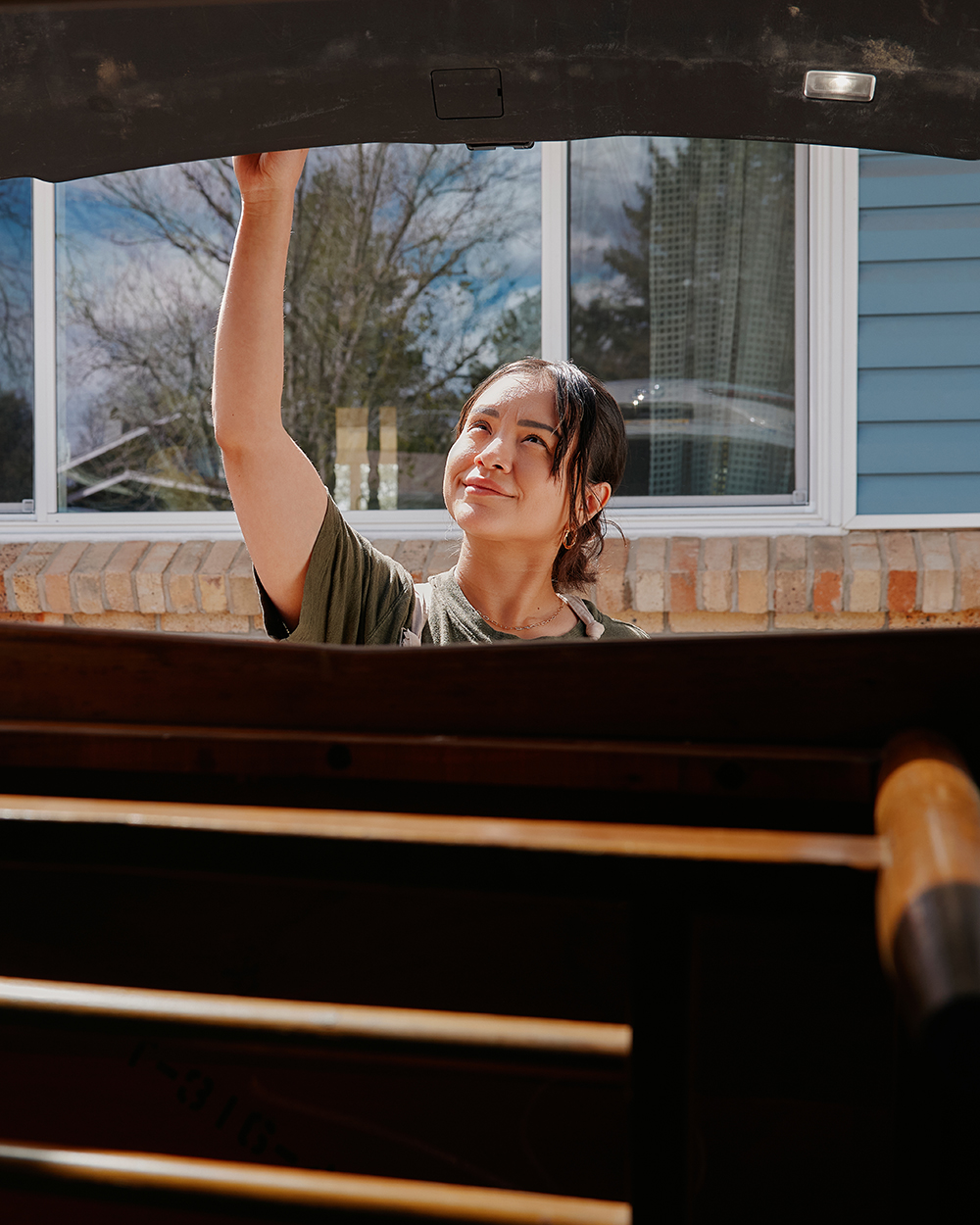 Woman lifting a small wooden table from the trunk of a vehicle parked outside a house