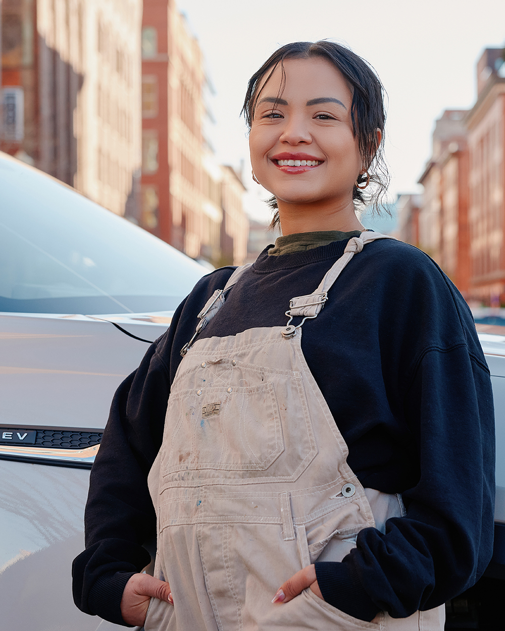 Woman smiling confidently while standing beside a white electric vehicle on a city street