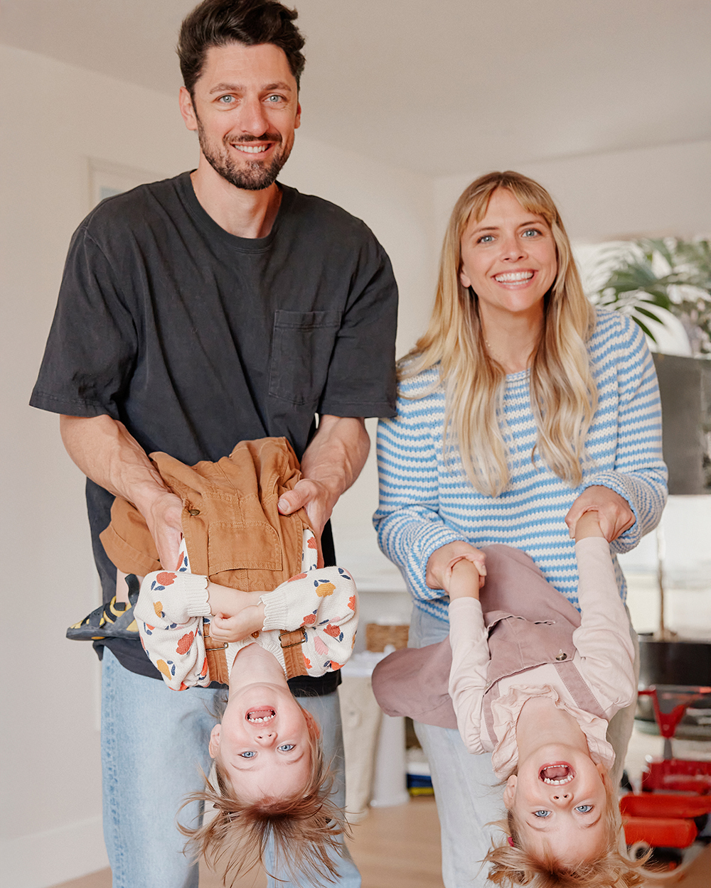 Smiling couple holding their two young daughters upside down while playing at home