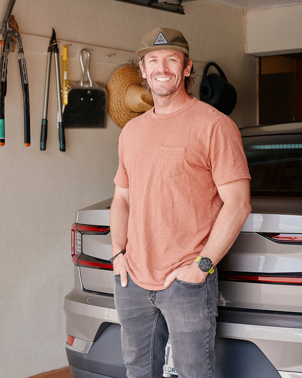 Man standing in front of an electric vehicle inside a garage, wearing a hat and casual clothes