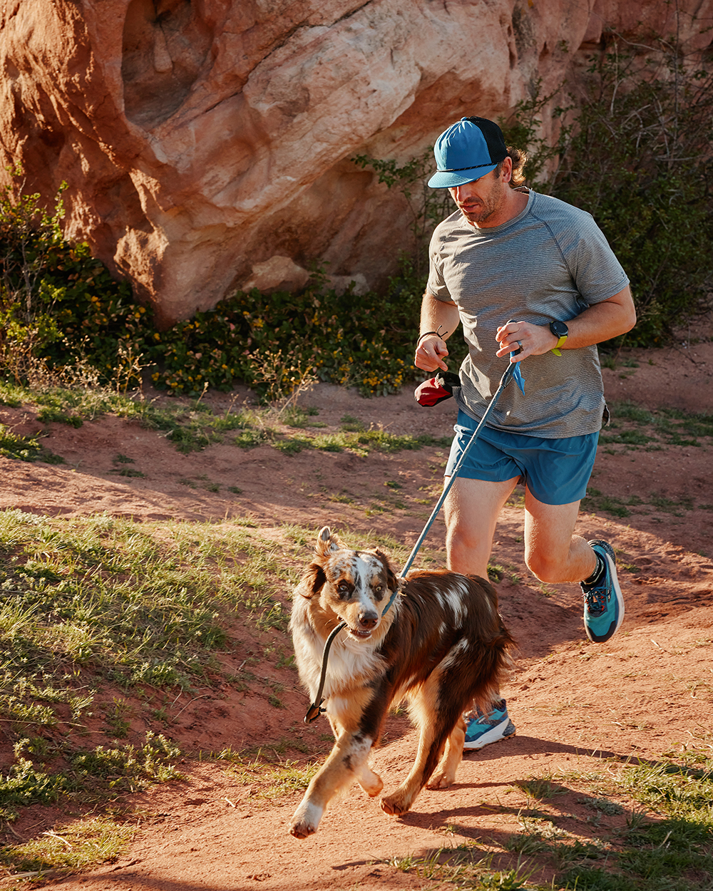 Man running on a dirt trail with his dog near red rock formations