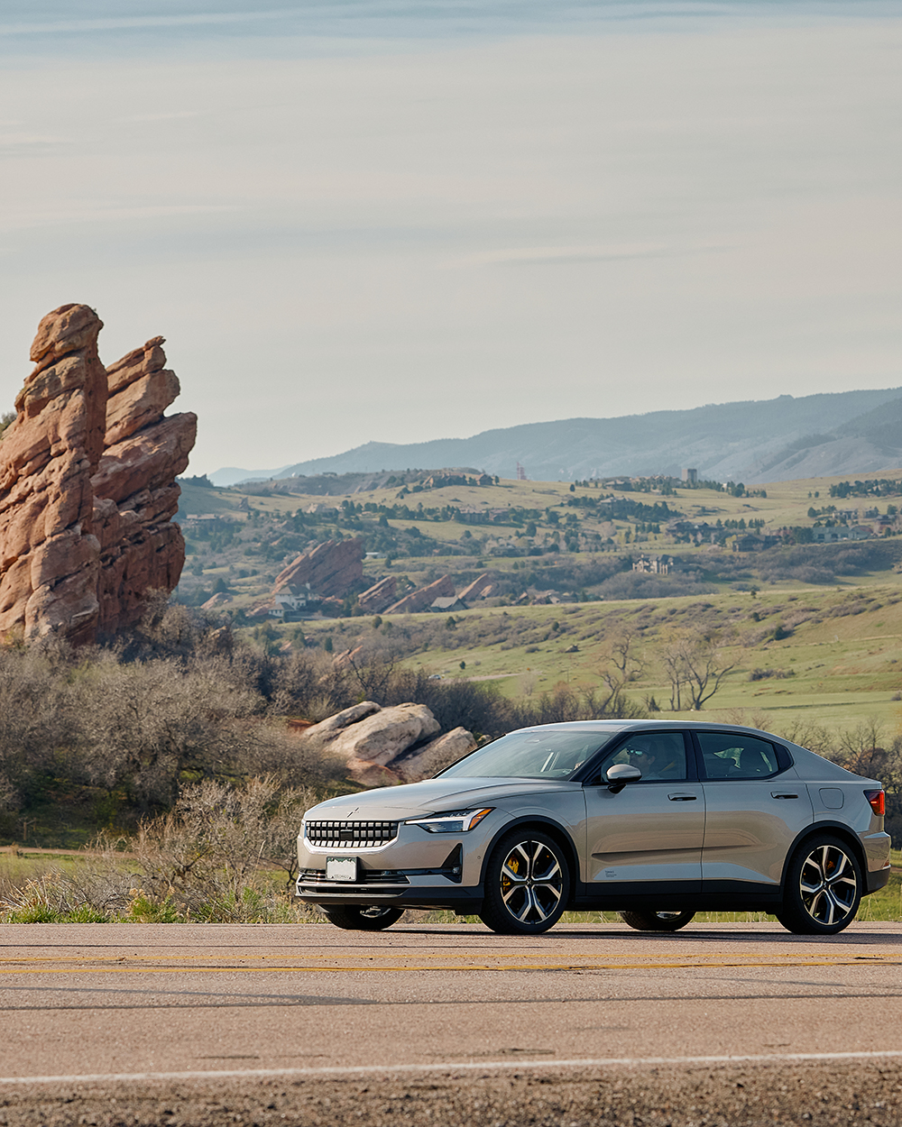 Electric vehicle driving along a road with large red rock formations and rolling green hills in the background