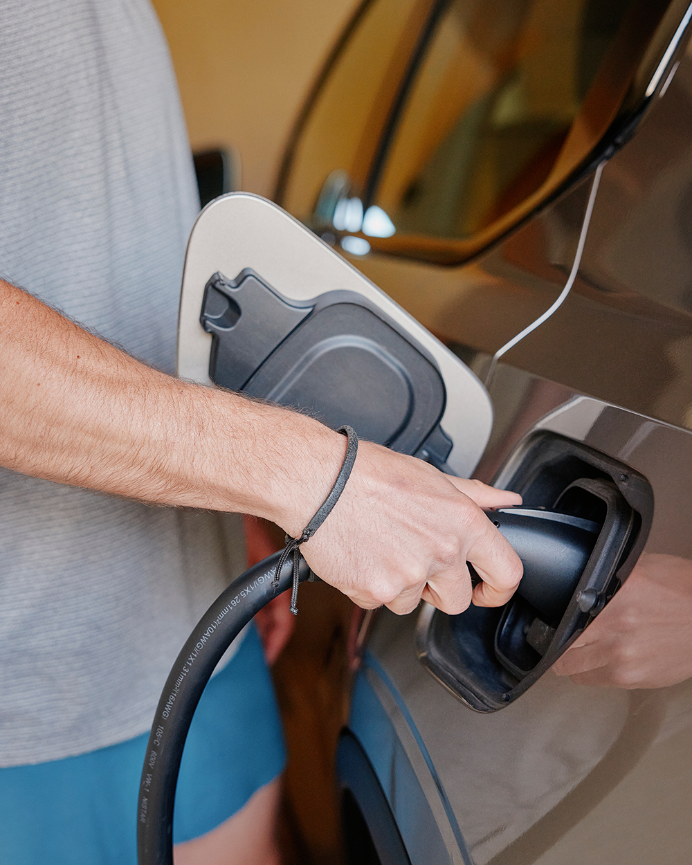 Close-up of a man plugging a charger into an electric vehicle in a garage