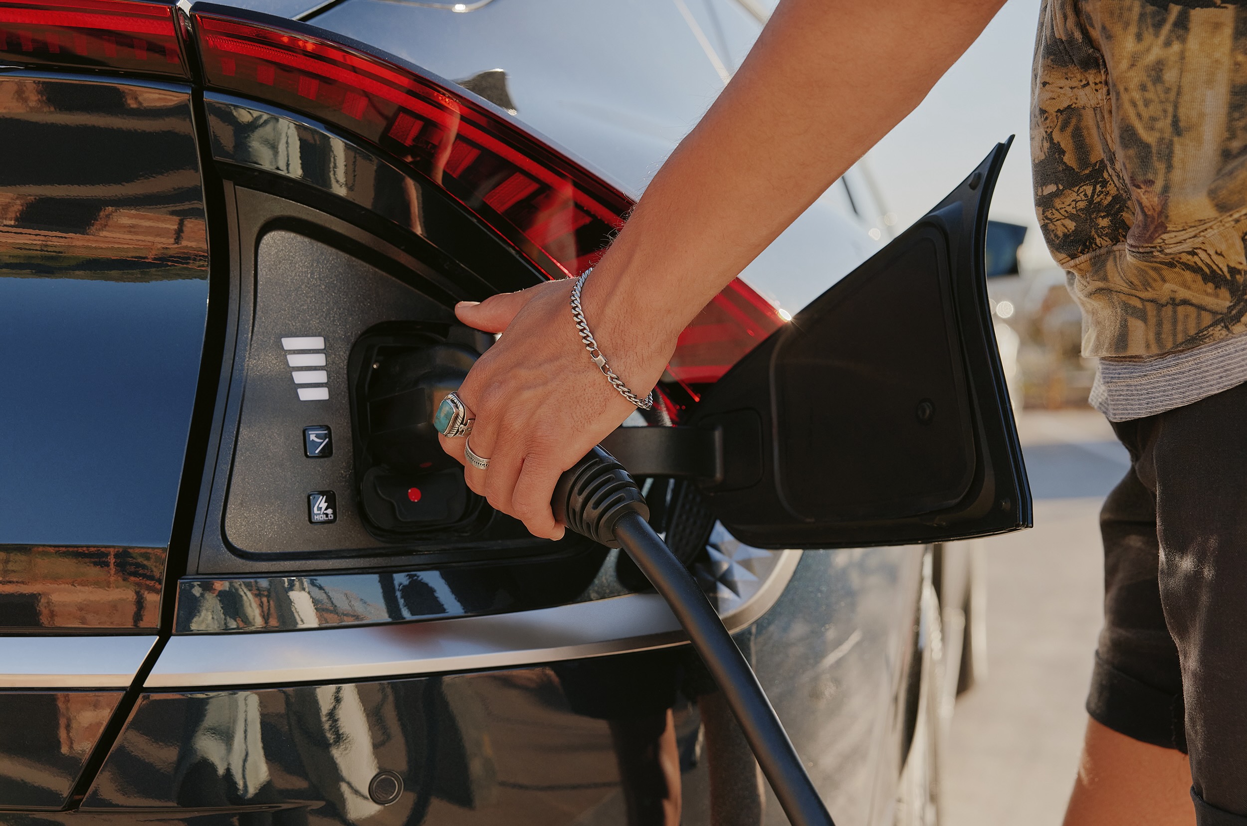 A person's hand plugs a charger into an electric vehicle.