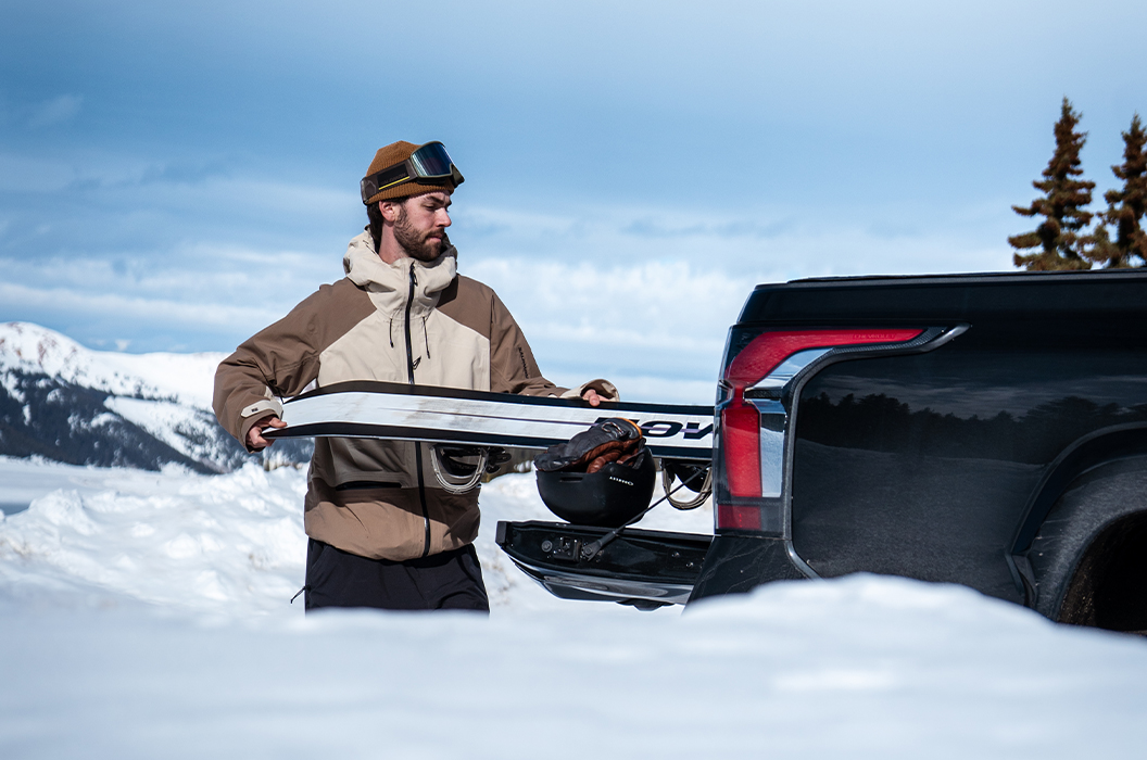 Snowboarder Ryan Wachendorfer loading a snowboard into the trunk of his Chevy Silverado EV.