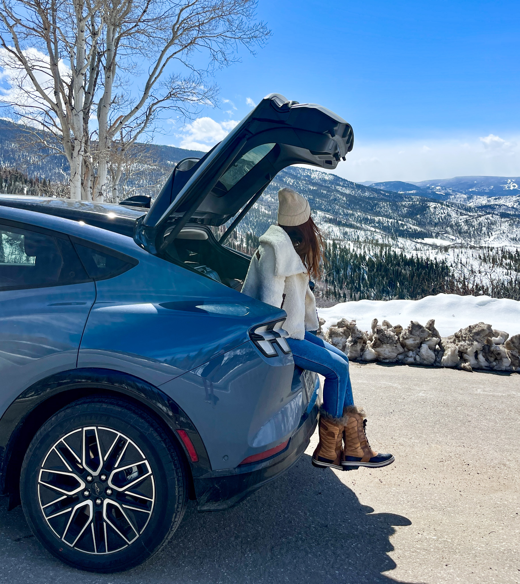 Amanda Bittner sitting in the truck of her gray Ford Mustang Mach-E EV, looking out over the Rockies in winter.