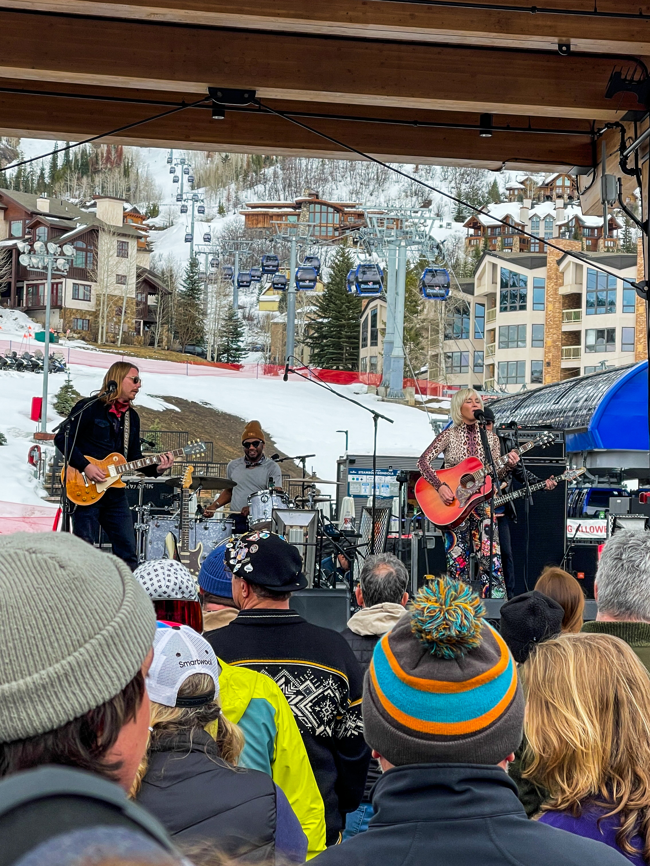 An outdoor concert in Steamboat Springs, played by a four-piece band with a woman singing. The ski lift can be seen in behind the stage, as can the resort’s hotels.