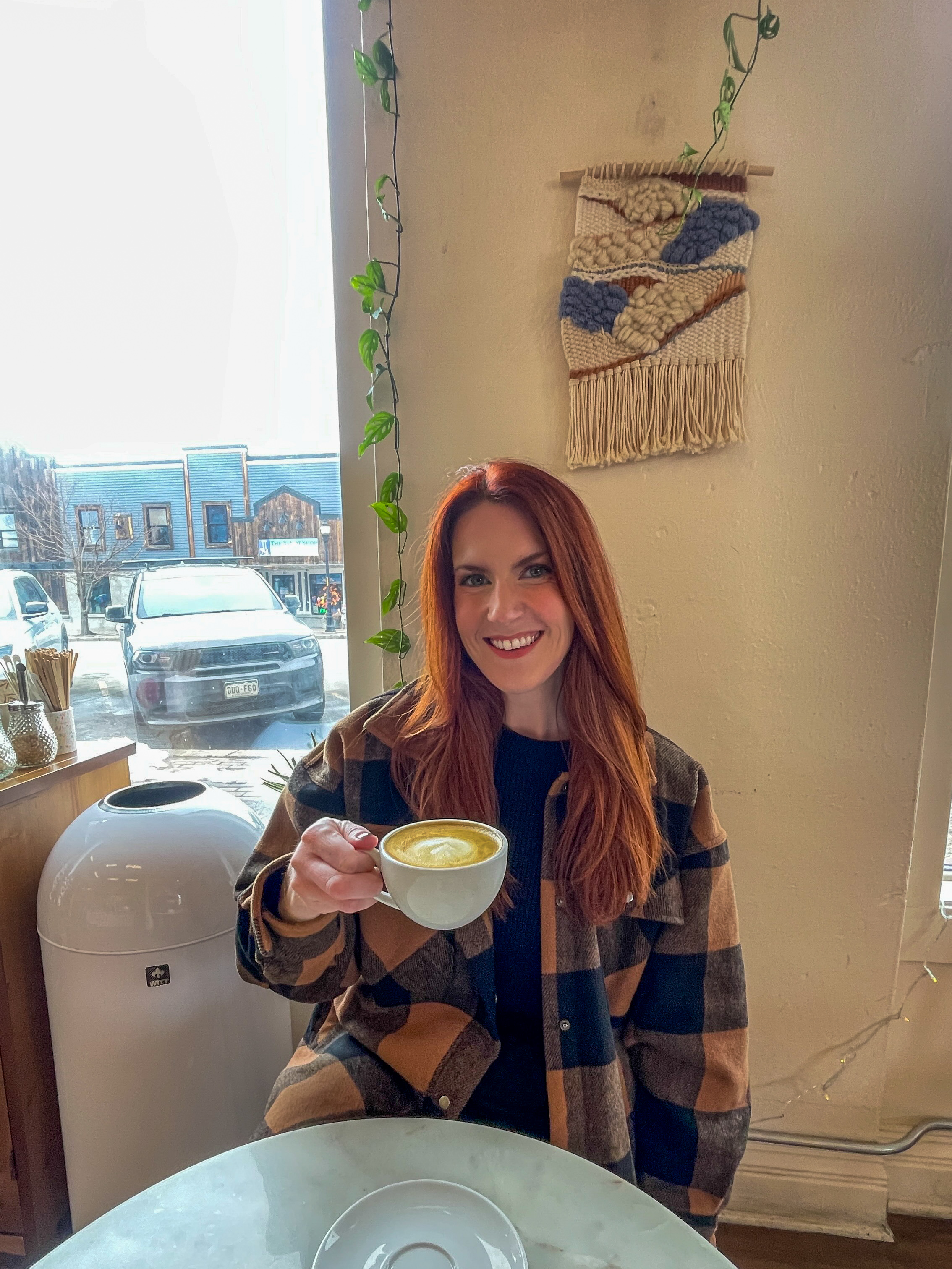 Amanda Bittner enjoys a latte at brunch. She has long auburn hair and is wearing a black and tan flannel coat.