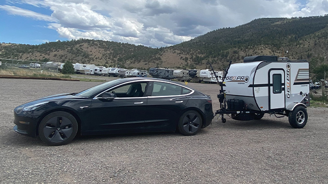 An image of Aaron's black Tesla Model 3 pulling a small camping trailer with mountains in the distance.