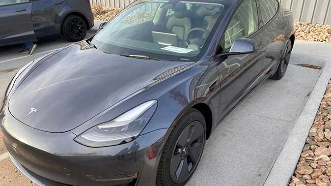 A close-up of the driver's side of Abraham's grey Tesla Model 3 parked.
