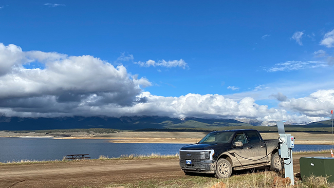 A picture of Benjamin's Ford F-150 Lightning charging on a dirt road after having off-roaded, in front of a lake.