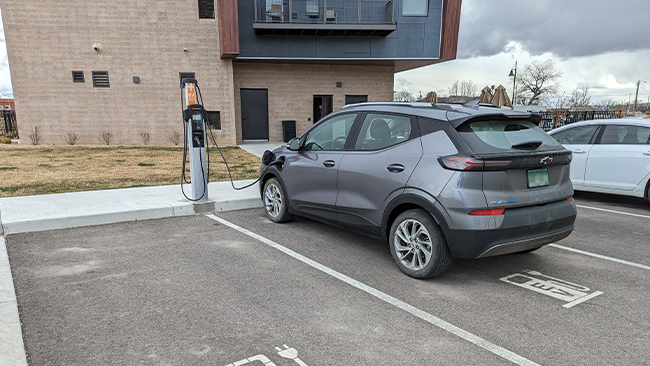A picture of Bryce's grey Chevy Bolt EUV charging in a parking lot in front of a condo building.