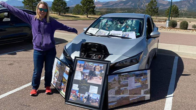 A picture of Caroline celebrating with her silver Nissan Leaf, with three framed picture collages featuring a summer road trip.