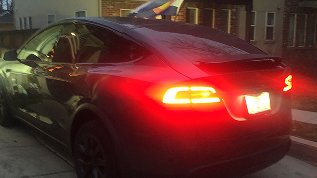 An image of Myron's Tesla Model X at dusk, with the brake lights illuminating the scene with a red glow.