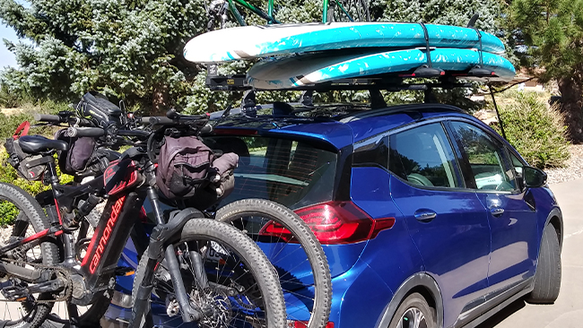 A picture of Stan's blue Chevy Bolt loaded with two paddleboards and two bikes in preparation for a lake trip.