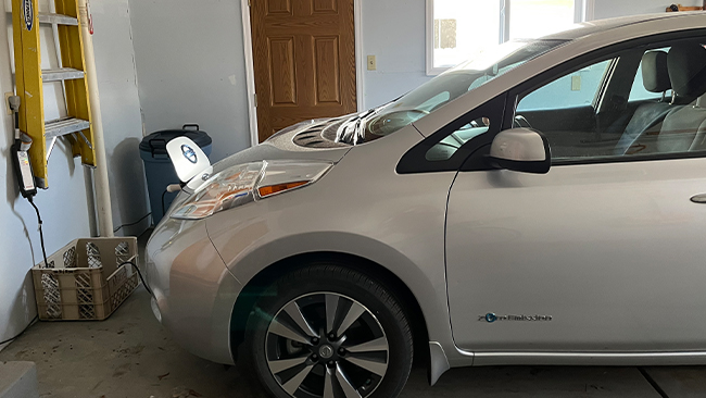 An image of Therese's pearl Nissan Leaf being charged in a home garage.