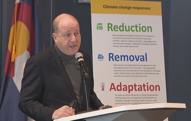 Govorner Jared Polis speaking from a lectern about Colorado's continued efforts to achieve its climate goals