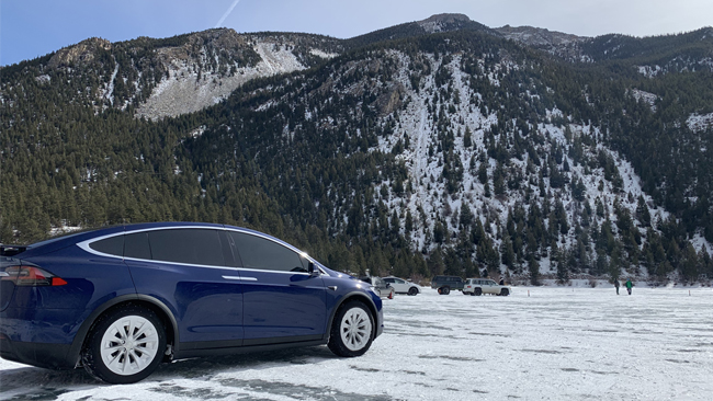 An image of Laura's Tesla Model X with tree-covered mountains with a light dusting of snow in the background.