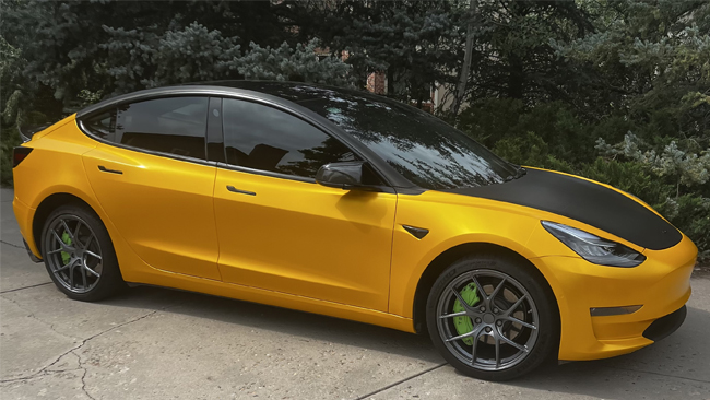 An image of Mark's parked goldenrod Tesla Model 3 from the right.