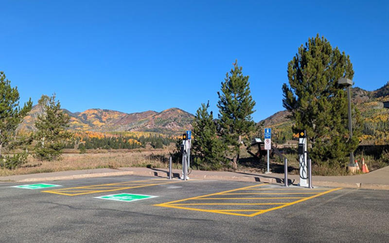 Parking lot with electric vehicle chargers. Trees and mountains are in the background.