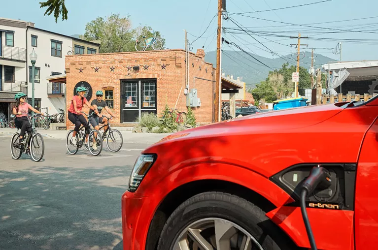 A red electric vehicle charging with bikers in the background.