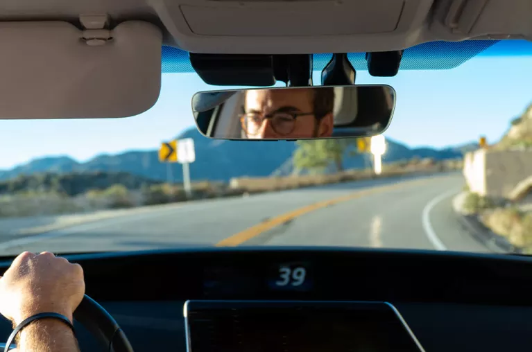 An image of a car from the back seat, seeing the driver's console and a driver through the rearview mirror.