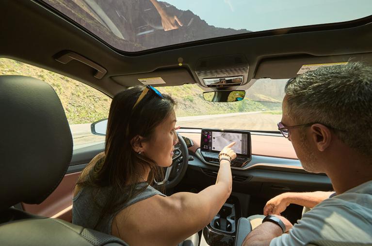 A couple pointing at the dashboard screen of a vehicle.