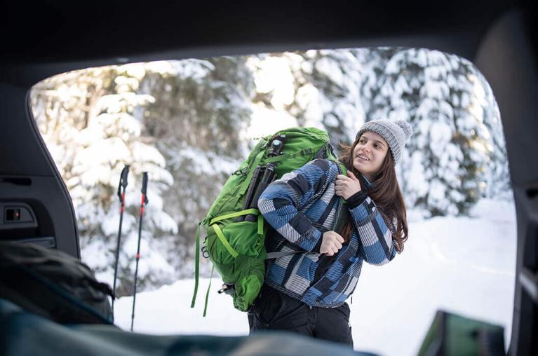A view of a woman with a backpack prepared to go hiking from a car window.