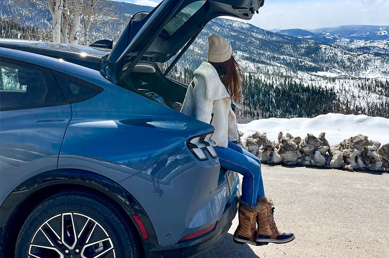 Amanda Bittner sitting in the truck of her gray Ford Mustang Mach-E EV, looking out over the Rockies in winter.